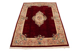 Savonnerie design rug corner, featuring black cherry red field, floral border, and ivory fringe.