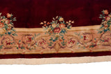 Scrolling border of rose bouquets and vinery, black cherry red field, ivory fringe.