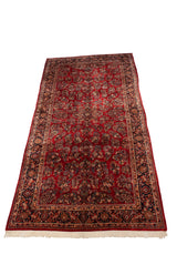 Angled view of a vintage Sarouk carpet, displaying the full length of its red floral field and border.
