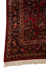 Corner detail of a vintage Sarouk carpet with its intricate navy blue border and clean ivory fringe.