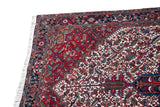 Corner of a vintage Mehrivan carpet showing the navy blue geometric border, side cord selvage, and ivory fringe.