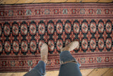 A person's perspective looking down at a Bokhara runner's repeating gul medallions in rust and ivory.