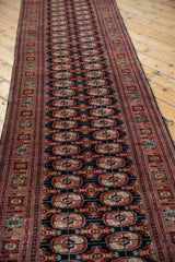 Angled view of a vintage Bokhara runner's lustrous pile and repeating rust and ivory gul medallions.