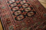 Angled view of the intricate multi-banded border and plush, high-sheen pile of a Bokhara rug.