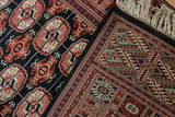 A corner of a vintage Bokhara rug runner showing the intricate border, plush field, and ivory fringe.