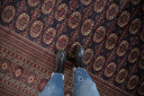 Detailed view of the plush pile and repeating red gul medallions on a navy Bokhara carpet.
