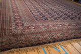The intricate geometric borders and high-sheen pile of a vintage Bokhara carpet shown from a corner angle.