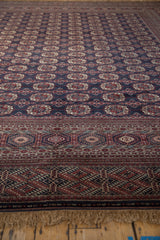 Angled view of a vintage Bokhara's intricate border, navy gul medallions, and plush wool pile.