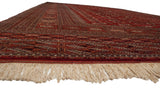 Low angle view of a vintage Bokhara carpet's lustrous red pile and intact ivory fringe.