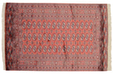 Rows of detailed gul medallions in navy and ivory on the dusty red field of a vintage Bokhara rug.