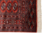 Detailed corner of a fine Bokhara rug showing its plush red pile, navy borders, and ivory fringe.