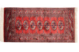 Vintage Bokhara rug corner showing plush red pile, geometric border, and ivory fringe.