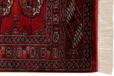 Plush red Bokhara rug pile, showing navy and ivory gul medallions, fine border, intact selvage, and cream fringe.