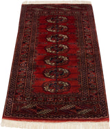 Vintage Bokhara rug corner showing red elephant footprint gul medallions, geometric borders, and white fringe.