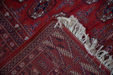 A folded corner on the vintage Bokhara rug shows its flat woven kilim end and ivory fringe.