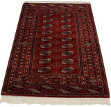 Detailed Bokhara rug section featuring cherry red field, navy gul medallions, and geometric border.