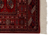 Corner of a fine Bokhara rug, with cherry red gul motifs, navy border, and ivory fringe.