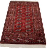 Secured end of the vintage Bokhara rug with ivory fringe and cherry red geometric borders.