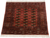 A vintage Bokhara rug from an angle, highlighting the sheen across its geometric gul pattern.