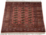 Angled view of a vintage Pakistani Bokhara rug, showing the geometric gul pattern on a dusty rose field.