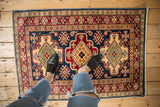 Person's feet on a low pile Pakistani Caucasian rug with vibrant geometric motifs.