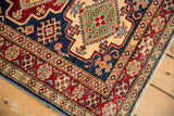 Geometric floral border, gem-like indigo, cherry red, saffron, on a Pakistani Caucasian rug.