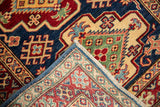 Hand knotted geometric wool pile in indigo, red, and ivory, revealing woven back and selvage.