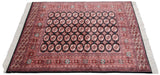 Angled view of a vintage Bokhara carpet highlighting the lustrous pile of its rust and black gul pattern.