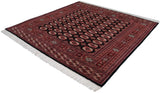 Angled view of a fine Bokhara square rug with rust and ivory gul medallions on a black field.