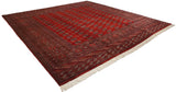 The lustrous red pile and geometric gul pattern of a fine Bokhara square carpet from an angle.