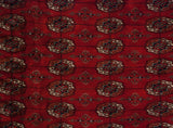 Detailed geometric gul medallions in navy, rust, and ivory on a plush cherry red Bokhara carpet.