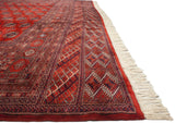 A fine Bokhara rug's detailed border and clean ivory fringe, viewed from a low side angle.