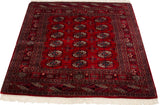 Angled view of a vintage square Bokhara rug showing its lustrous red pile and geometric gul design.