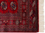 Fine corner detail of a vintage Bokhara rug with intricate geometric borders and ivory fringe.