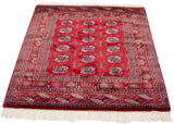 Vintage fine Bokhara rug from an angle, displaying its repeating gul pattern and ivory fringe.