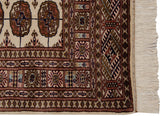 Corner of a vintage Bokhara rug showing its intricate border, original side selvage, and soft ivory fringe.