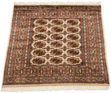 A vintage square Bokhara rug's plush, lustrous pile and repeating gul motifs seen from an angle.
