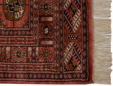 Vintage Bokhara rug corner with dusty rose geometric gul pattern and original ivory fringe.