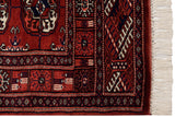 Corner of a vintage Bokhara rug showing its geometric border, red selvage, and clean fringe.