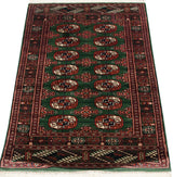 Angled perspective of a vintage Bokhara rug with a lustrous green pile and repeating gul pattern.