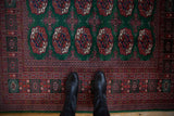 Detail of the fine Bokhara rug's repeating gul medallions on a green field beside the intricate rust border.