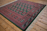 Angled view of a vintage Bokhara rug showing its lustrous pile and intricate green and red pattern.
