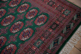 Detailed geometric border and clean ivory fringe on the corner of a plush vintage green Bokhara rug.