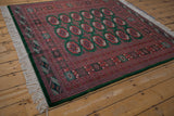 Angled view of a vintage Bokhara rug showing its geometric border, green pile, and ivory fringe.