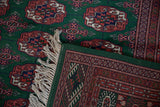 Detail of a vintage Bokhara rug's corner, showing the intact green side cord selvage and ivory fringe.
