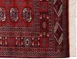 The intricate geometric border and clean ivory fringe of a vintage hand-knotted Bokhara rug.