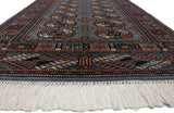 Low angle of a vintage Bokhara rug showing its plush pile, repeating guls, and ivory fringe.