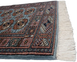 Corner detail of a plush Bokhara rug with its intricate border and clean ivory fringe.