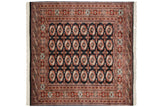 Detailed repeating gul medallions in rust and ivory on the dark field of a fine Bokhara carpet.