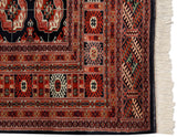 Corner detail of a fine Bokhara rug showing its intricate geometric borders, dark selvage, and ivory fringe.